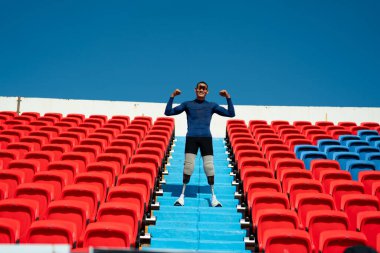 Stadyumdaki koşu pistinde protez bıçaklı Asyalı atletler. Futbol stadyumundaki koltuklar