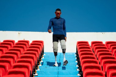 Stadyumdaki koşu pistinde protez bıçaklı Asyalı atletler. Futbol stadyumundaki koltuklar