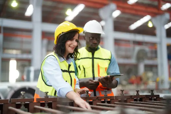 Modern fabrikanın üretim bölümünde iş tulumu ve şapka giyen ve fikirleri tartışan iki profesyonel teknisyen.  