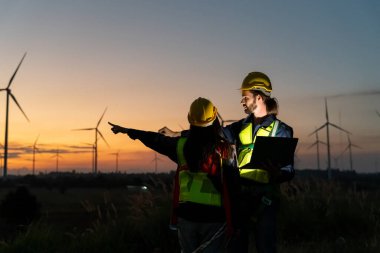 Rüzgar türbinlerini inceleyen iki çok ırklı sanayi işçisi. Üretim ekosistemi temiz yeşil enerjili kırsal alan