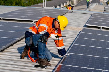 Uzman teknisyen profesyonel mühendis güneş ışığı altında fabrikanın çatısına güneş paneli kurarken üst görüntüyü kontrol ediyor. Elektrik yenilenebilir eko enerji hizmeti veren mühendisler