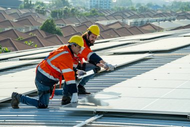 Uzman teknisyen profesyonel mühendis güneş ışığı altında fabrikanın çatısına güneş paneli kurarken üst görüntüyü kontrol ediyor. Elektrik yenilenebilir eko enerji hizmeti veren mühendisler