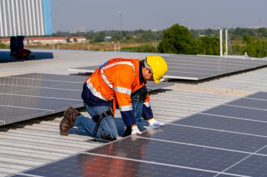 Profesyonel mühendis güneş ışığı altında fabrikanın çatısındaki güneş panelini kontrol ediyor. Elektrik yenilenebilir eko enerji hizmeti veren bir mühendis.