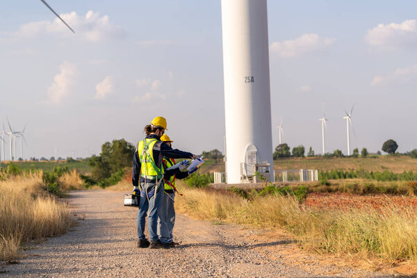 Two multiracial industrial workers examining wind turbines. Rural area with eco farm of production clean green energy