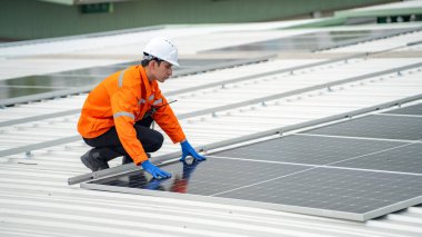 Evin çatısına fotovoltaik güneş modülleri monte eden bir inşaatçı. Güneş paneli sistemi kuran miğferdeki insan mühendisin arka görüntüsü. Alternatif ve yenilenebilir enerji kavramı.