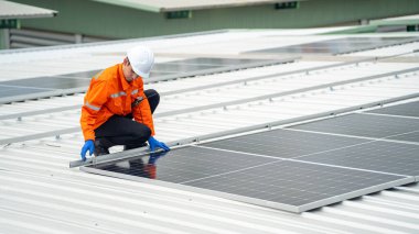 Evin çatısına fotovoltaik güneş modülleri monte eden bir inşaatçı. Güneş paneli sistemi kuran miğferdeki insan mühendisin arka görüntüsü. Alternatif ve yenilenebilir enerji kavramı.