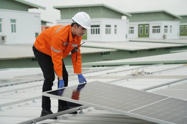 Evin çatısına fotovoltaik güneş modülleri monte eden bir inşaatçı. Güneş paneli sistemi kuran miğferdeki insan mühendisin arka görüntüsü. Alternatif ve yenilenebilir enerji kavramı.
