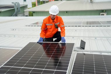 Evin çatısına fotovoltaik güneş modülleri monte eden bir inşaatçı. Güneş paneli sistemi kuran miğferdeki insan mühendisin arka görüntüsü. Alternatif ve yenilenebilir enerji kavramı.