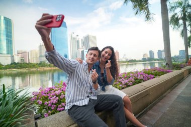 Bangkok, Tayland 'da bir köprüde otururken cep telefonuyla selfie çeken mutlu çift.