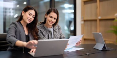 Genç bayan yönetici ve Asyalı genç iş kadını modern ofiste bilgisayarla birlikte çalışıyorlar.
