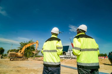 İnşaat alanında duran üniformalı iki inşaat işçisi.