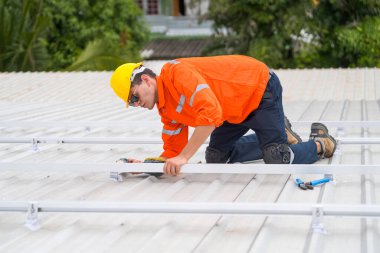 Erkek teknisyenler fotovoltaik güneş modüllerini evin çatısına monte ediyorlar..