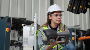 Kadın teknisyen dijital tabletli bir robot kolu programlar ve bir fabrikada robot montajlar.