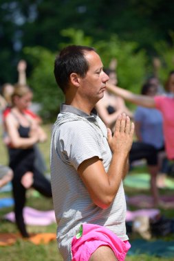 Şehir parkında yoga yapan bir adam, arka planda meditasyon yapan bir grup insan. 12 Temmuz 2020. Kiev, Ukrayna