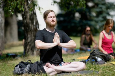 Şehir parkında yoga yapan bir adam, arka planda meditasyon yapan bir grup insan. 12 Temmuz 2020. Kiev, Ukrayna