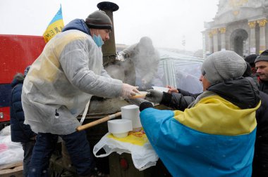 Erkek aşçı, ocaktan kadına yemek veriyor, insanlar sırada bekliyor. Çadır kasabası, Haysiyet Devrimi. 7 Aralık 2013. Kyiv, Ukrayna