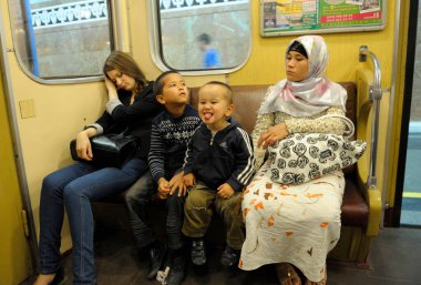 Asyalı genç bir kadın ve metro vagonunda bankta oturan iki küçük çocuk. 5 Eylül 2019. Kyiv, Ukrayna