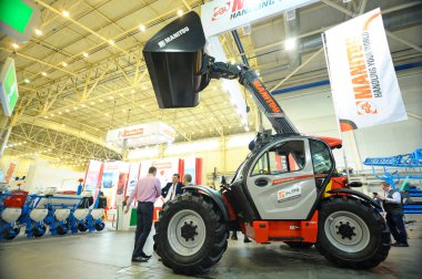 Mini kepçenin yeni modeli bir tezgahta sunuluyor, insanlar etrafta dolaşıyor. Sergi AgroTrade Show-2019. 19 Şubat 2019. Kyiv, Ukrayna