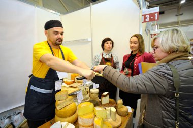 Erkek satıcı bir kadına tadına bakması için bir dilim peynir veriyor. 29 Kasım 2019. Kyiv, Ukrayna