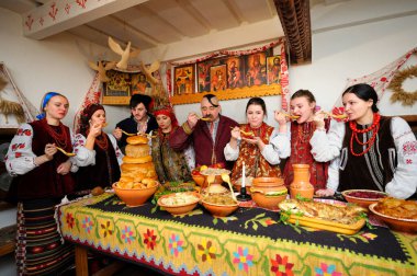 Ukrayna yerlisi kostümlü aile Noel arifesini kutlamak için geleneksel tabaklarla masanın arkasında toplandı. Ukrayna gelenekleri, yeniden yapılanma. 4 Ocak 2018. Kyiv, Ukrayna