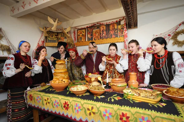Ukrayna yerlisi kostümlü aile Noel arifesini kutlamak için geleneksel tabaklarla masanın arkasında toplandı. Ukrayna gelenekleri, yeniden yapılanma. 4 Ocak 2018. Kyiv, Ukrayna