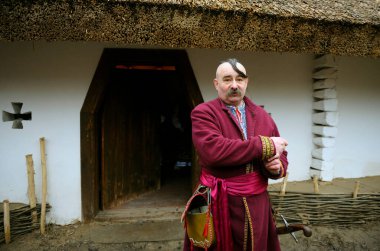 Kazak ve kılıçtan oluşan Ukrayna yerlisi kostümlü bir adam kırsal evinin önünde duruyor. Ukrayna gelenekleri, yeniden yapılanma. 4 Ocak 2018. Kyiv, Ukrayna