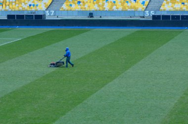 İşçi çim biçme makinesi, çim biçme makinesiyle futbol sahasında çim biçiyor. Kyiv, Ukrayna