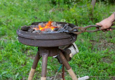 Demirci el, yanan bir demir ocağında metal bir çubukla pensleri tutuyor..