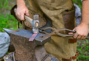 Demircilerin elleri forseps ve çekiç tutuyor. Metal bir çubuk dövüyor, bıçak gibi, örsün üzerinde..
