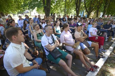 Bir grup hamile kadın ve kocaları banklarda oturmuş şehir parkındaki konuşmacıları dinliyorlar. 25 Haziran 2019. Kyiv, Ukrayna