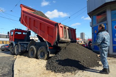 Çöp kamyonu kaldırımları tamir etmek için zemin boşaltıyor. Adam işçi izliyor. 17 Mart 2021. Kyiv, Ukrayna