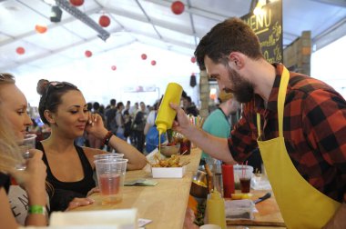 Tezgahta yemek pişirip ızgara sosu hazırlarken kadın müşteriler izliyor. Fast food festivali. 24 Nisan 2018. Kyiv, Ukrayna