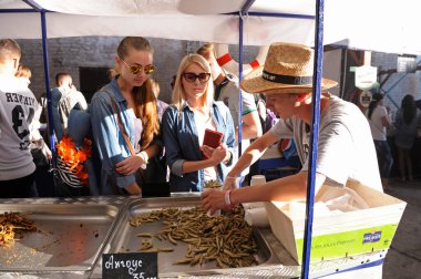 Tezgahta duran ve ançüezleri kağıt bardağa koyan satıcı, kadın müşteriler izliyor. Fast food festivali. 24 Nisan 2018. Kyiv, Ukrayna