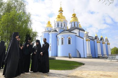 Kilisenin yanında duran bir grup keşiş, arka planda Aziz Michael Altın Kubbe Manastırı. 27 Nisan 2018. Kiev, Ukrayna