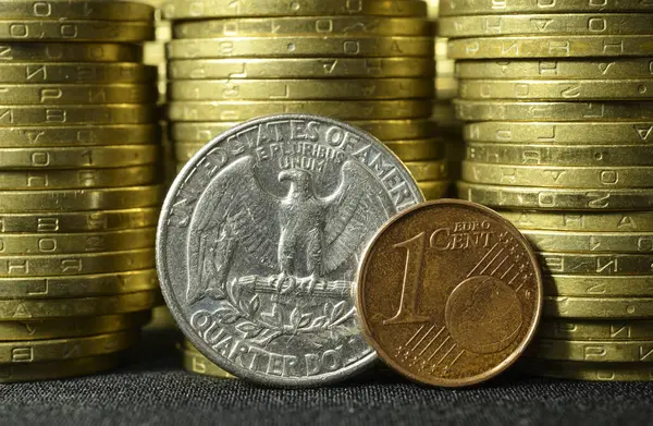 Quarter dollar coin and one euro cent coin placed on edges in front of coins