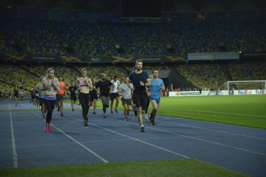 Bir grup koşucu akşam ışığında stadyumun raylarında koşuyor. 14 Ekim 2019. Olimpiyat Ulusal Spor Kompleksi, Kiev, Ukrayna