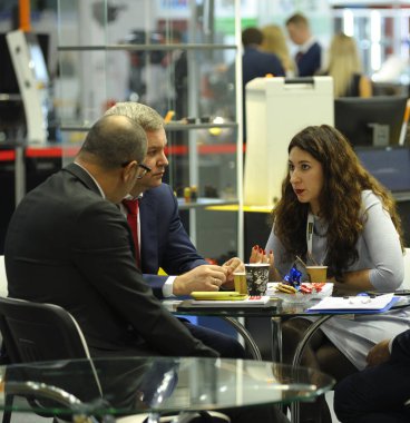 Diyalog kuruyorum. Kadın yönetici masada oturan iş adamlarıyla konuşuyor, insanlar arka planda yürüyor. Endüstri Sergisi. 19, 2019. Kiev, Ukrayna