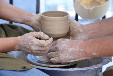 Tekerlek fırlatmayı öğretiyorum. Potter 'ın eli çömlekçinin tekerindeki kilin şeklini düzeltirken kadınlarınkini düzeltiyor..