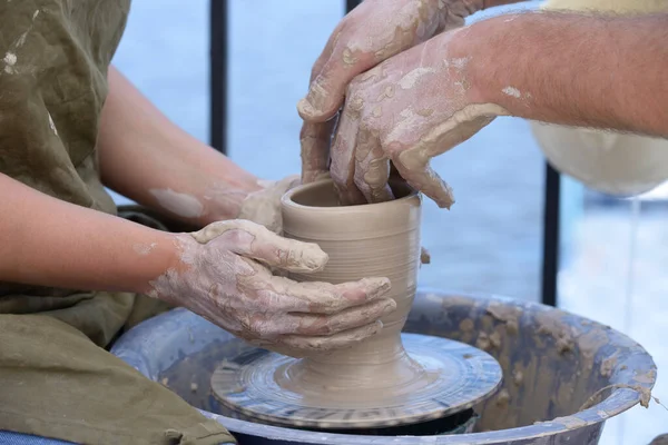 Teaching of wheel throwing. Potter hand correcting woman s ones during shaping clay blank on a potter's wheel.