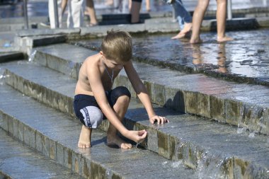 Küçük çocuk merdivenlerden aşağı akan çeşme suyuyla oynuyor. 5 Haziran 2019. Kiev, Ukrayna
