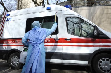 Sağlık görevlileri ambulans arabasını motorlu sırt çantası atomizleyicisi ve spreyiyle dezenfekte ediyorlar.