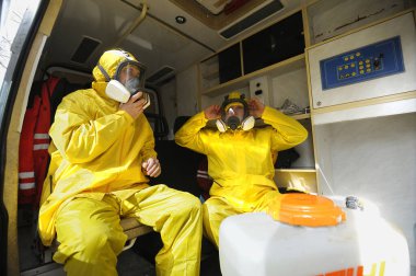 Ambulansta oturan sağlık görevlileri sarı koruyucu kostümler ve maskeler takarak Coronavirüs 'ü dezenfekte etmeye hazırlanıyorlar. 26 Şubat 2020. Kiev, Ukrayna