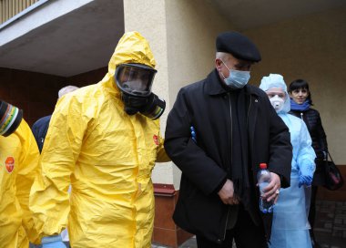 Sağlık görevlisi, maskeli yaşlı bir adama ambulans arabasından enfeksiyon hastalıkları departmanına, koronavirüse gitmesi için yardım ediyor. 26 Şubat 2020. Kiev, Ukrayna