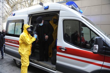 Sağlık görevlisi, maskeli yaşlı bir adama ambulans arabasından enfeksiyon hastalıkları departmanına, koronavirüse gitmesi için yardım ediyor. 26 Şubat 2020. Kiev, Ukrayna