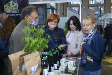 Erkek satıcı, kenevir kozmetik ürünlerinin önünde duran ve ön planda büyüyen üç kadınla konuşuyor. Esrar fuarı. 2 Ekim 2020. Kyiv, Ukrayna