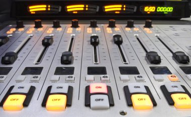 Düğmeler, ses seviyeleri, ses karıştırıcı kontrol paneli radyo stüdyosundaki bir masada çalışıyor.