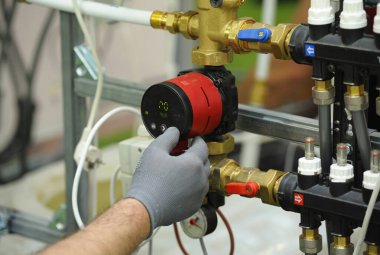 Tesisatçı eldiveni kazan pompasının ekranına dokunuyor..