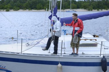 Yatçılar yelkenli bir yatın güvertesinde ellerinde halatlarla rıhtıma demirlemeye hazırlar. Şehir gününe adanmış amatör yelkenli yarışı. 30 Mayıs 2021. Kyiv, Ukrayna