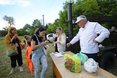 Aşçı seyyar mutfağın önünde duruyor ve tabağa bedava yemek koyuyor, bir grup insan bekliyor. Köyün günü. 12 Haziran 2021. Borysivka, Ukrayna