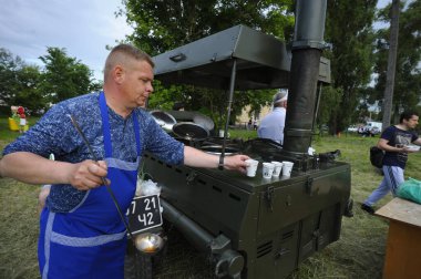 Aşçı seyyar mutfağın önünde duruyor ve kepçeli çayları bardaklara dolduruyor. Köyün günü. 12 Haziran 2021. Borysivka, Ukrayna